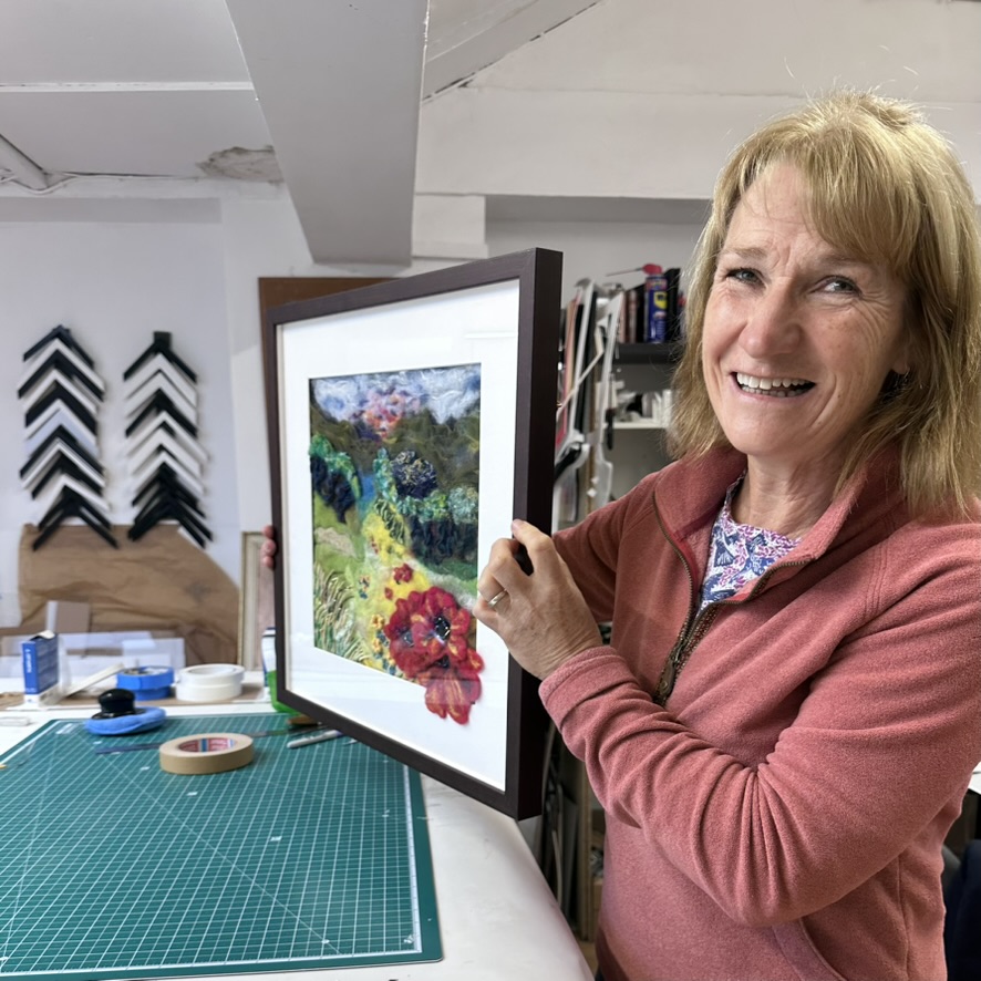 A smiling student holding the felt-flower artwork she framed at the Glasgow picture framing class